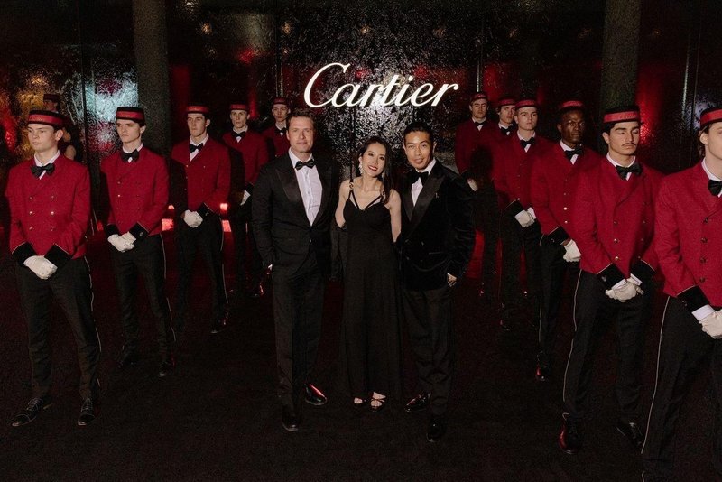 James Sackl and Alina Sackl with a guest at the Cartier Sydney gala, June 2026, flanked by Cartier's signature red-jacketed bellboys in front of the illuminated Cartier sign.