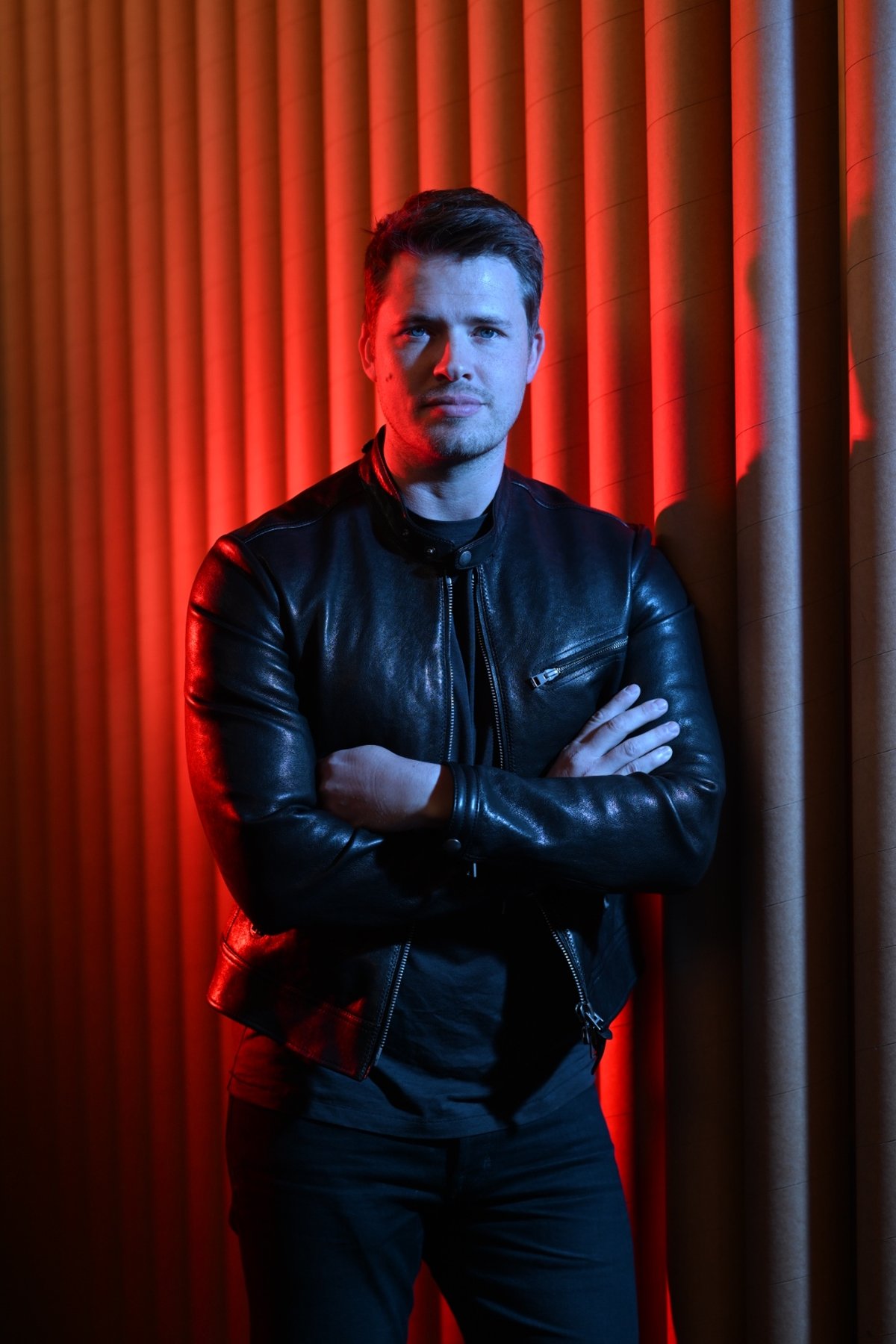 James Sackl, Melbourne founder of Wallace Biotechnologies and Terraform Technologies, full-length portrait in a black leather jacket against a red-lit ribbed backdrop.